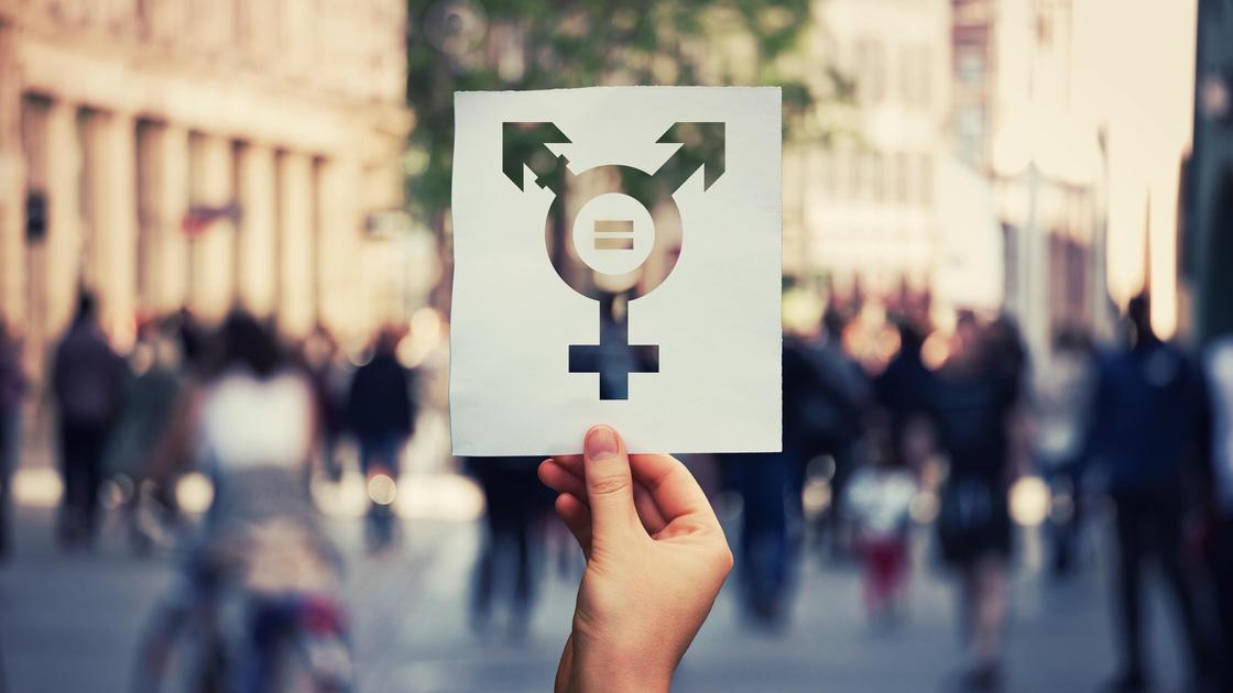Рука держит лист бумаги с трансгендерным символом и знаком равенства внутри