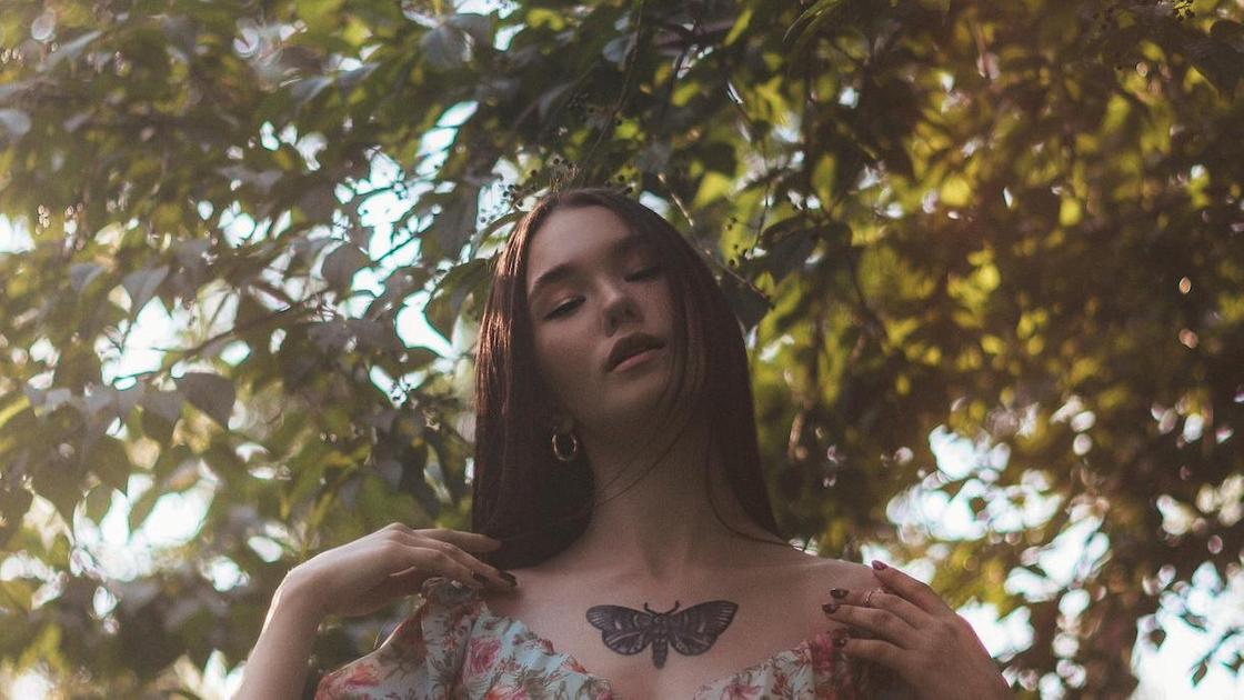 Девушка с татуировкой бабочки между ключицами