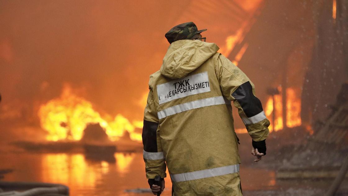 Пожарный стоит на фоне горящего здания