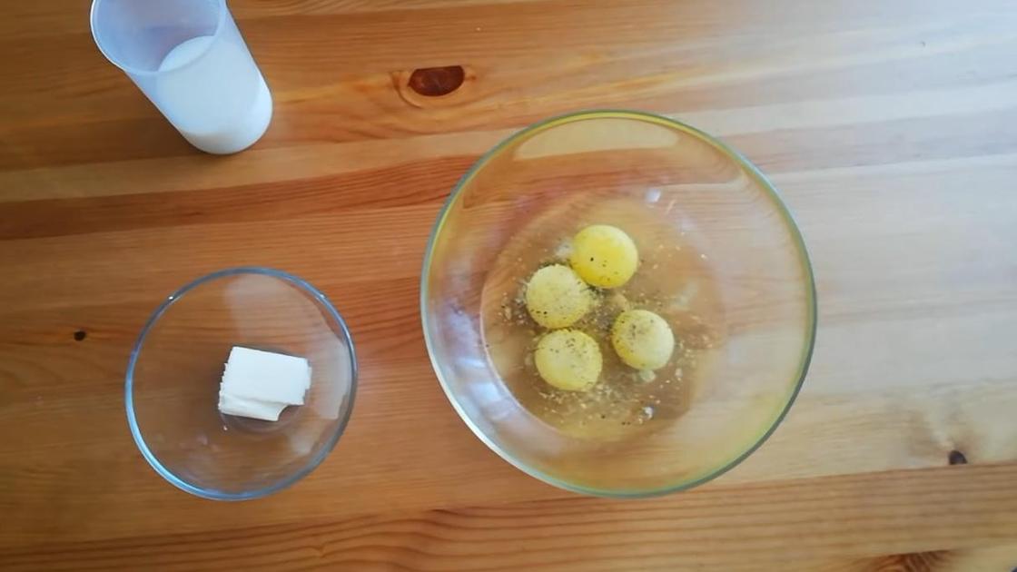 Разбитые в прозрачную миску яйца посыпаны черным перцем и солью