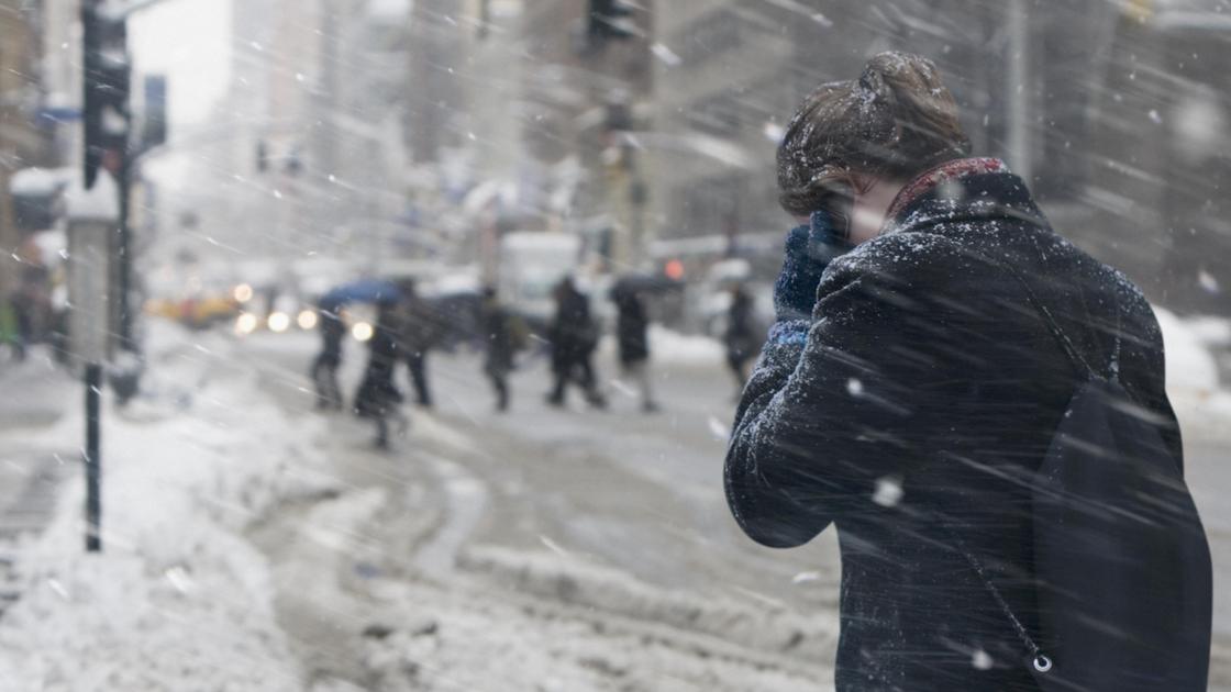Девушка закрывается от снега на улице города