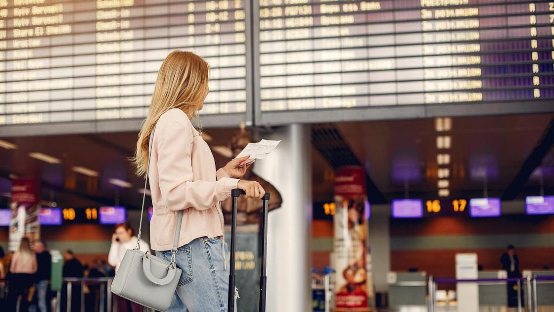 Девушка с чемоданом в аэропорту у табло с расписанием рейсов