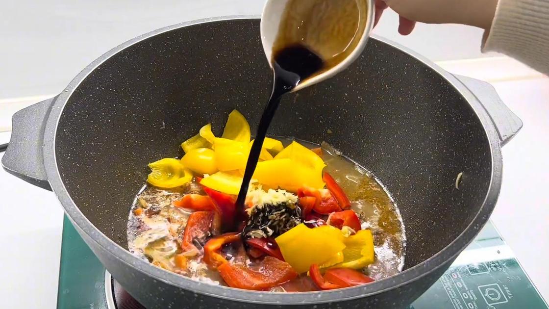 Соевый соус наливают из соусника в казан с тушеным мясом и овощами