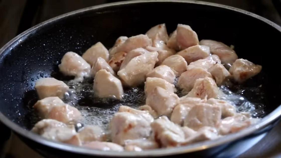 На сковороде жарятся кусочки курицы с чесноком