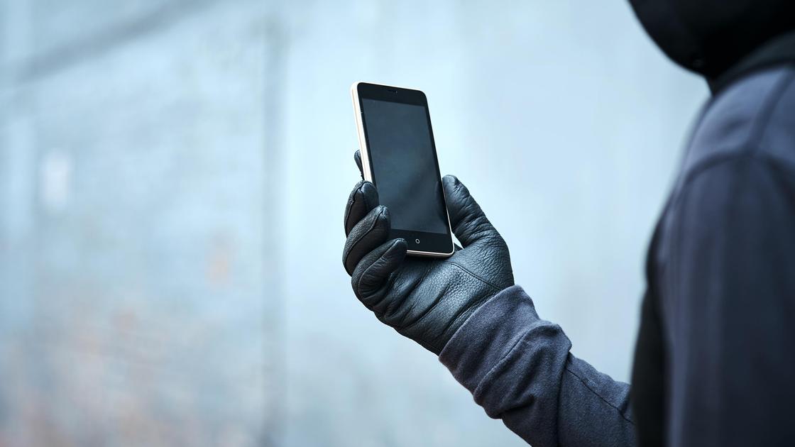 Мужчина в черной одежде и в перчатках держит в руке смартфон