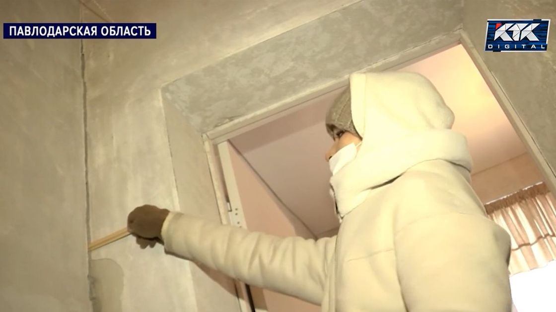 Женщина показывает трещины в доме