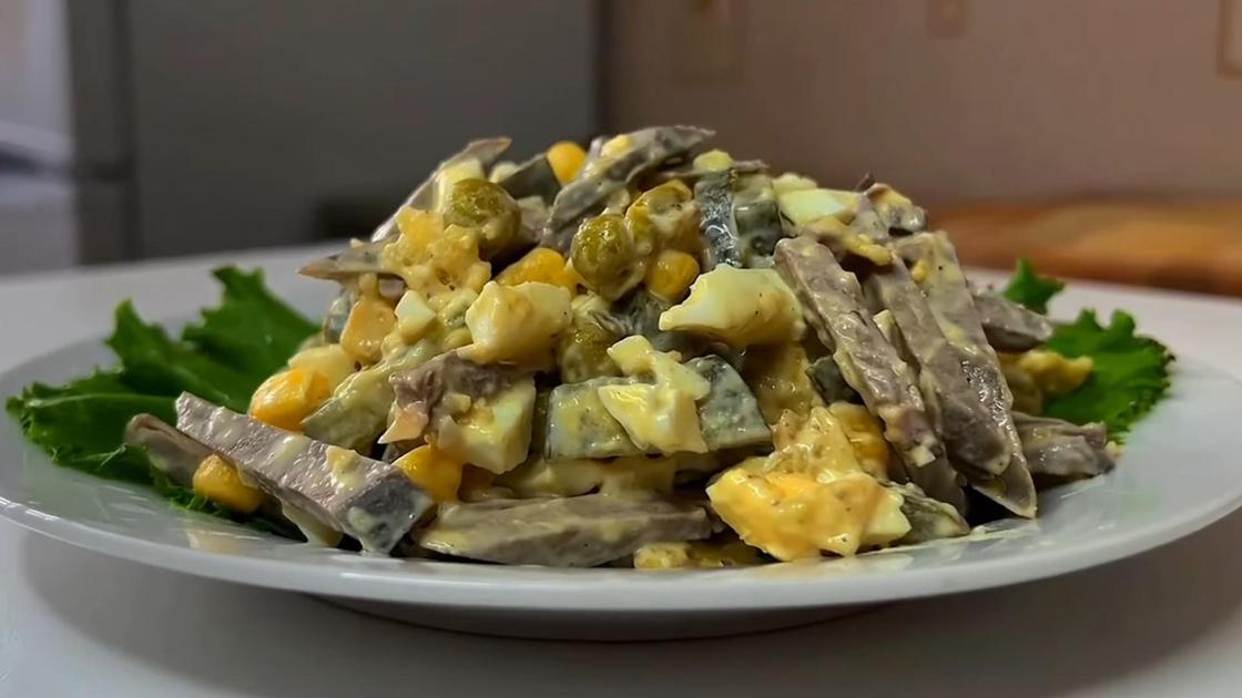 На сервировочной тарелке салат из печени, яиц, огурцов, кукурузы и горошка