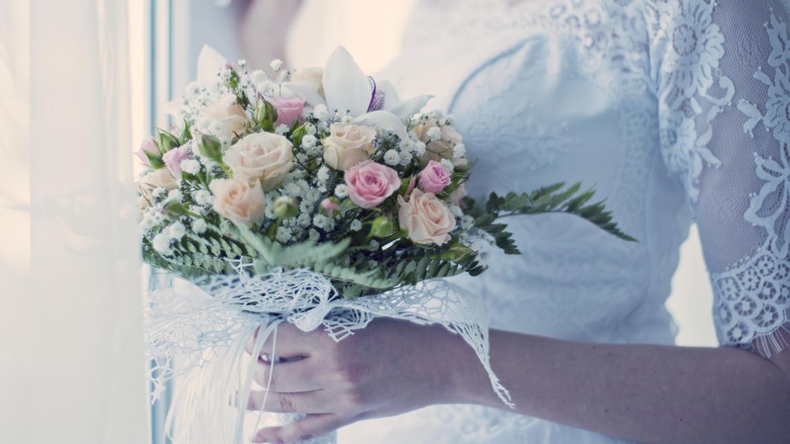 Невеста с букетом цветов стоит у окна