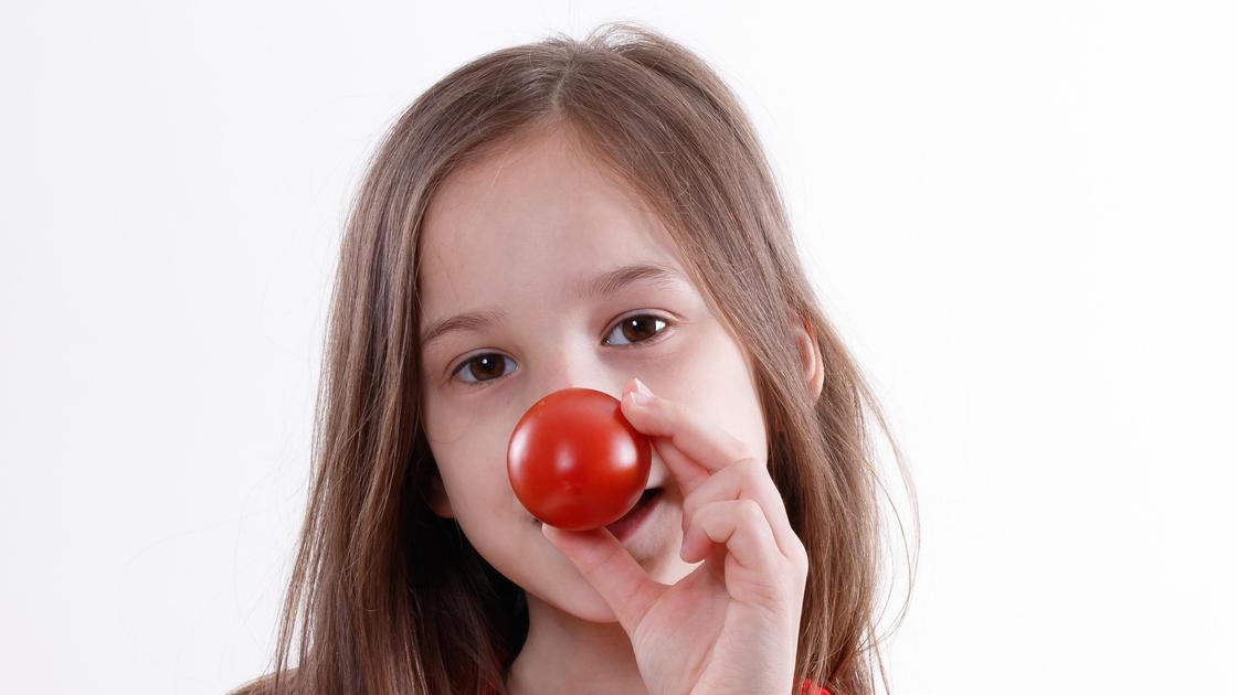 Девочка держит помидор около носа