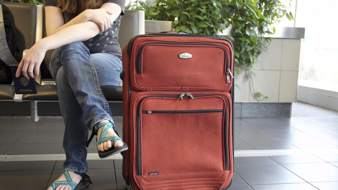 Девушка с красным чемоданом сидит в аэропорту