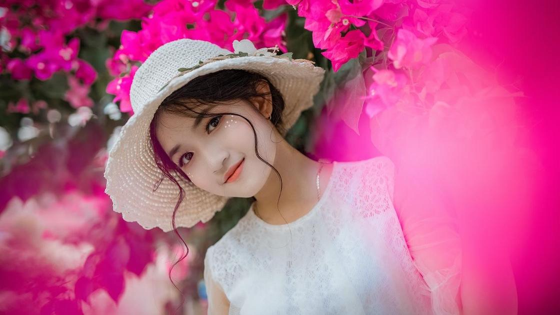 Красивая ухоженная девушка на фоне розовых цветов улыбвается