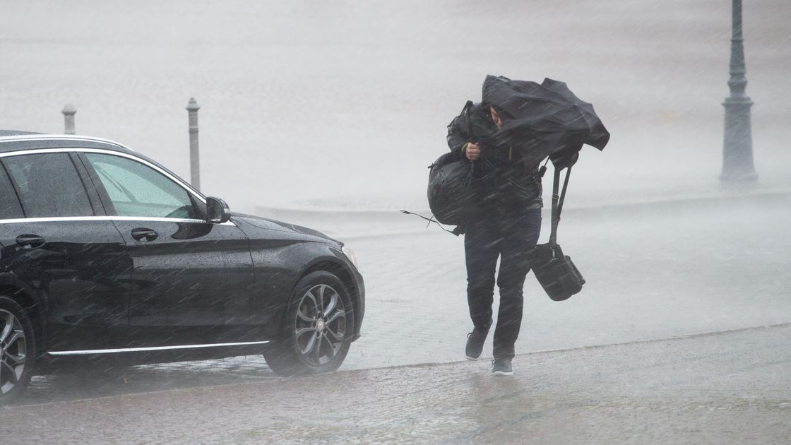 Мужчина прикрывается зонтом от дождя и ветра