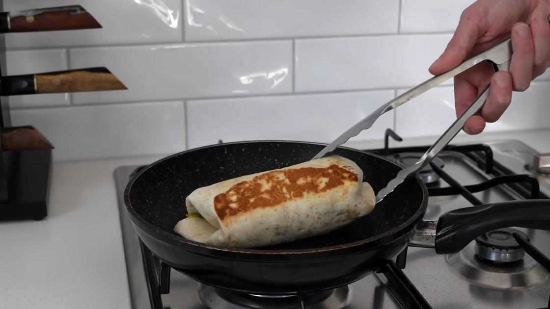 Обжаренный буррито переворачивают щипцами на сковороде