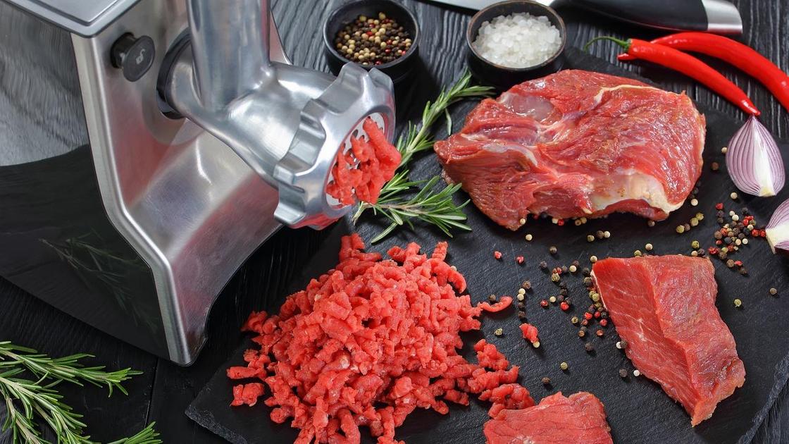 На столе стоит мясорубка и куски сырого мяса