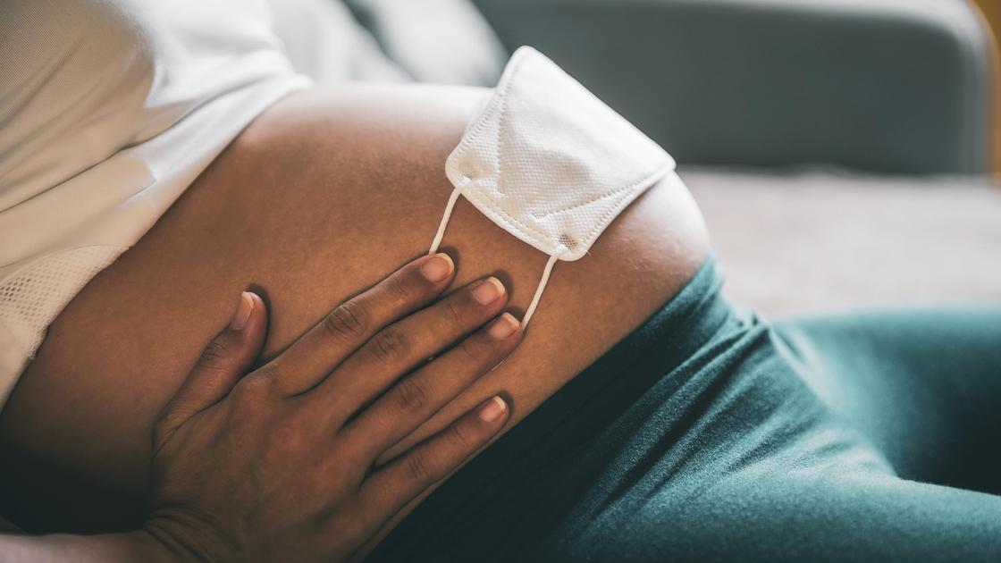 Беременная женщина держит руками медмаску на животе