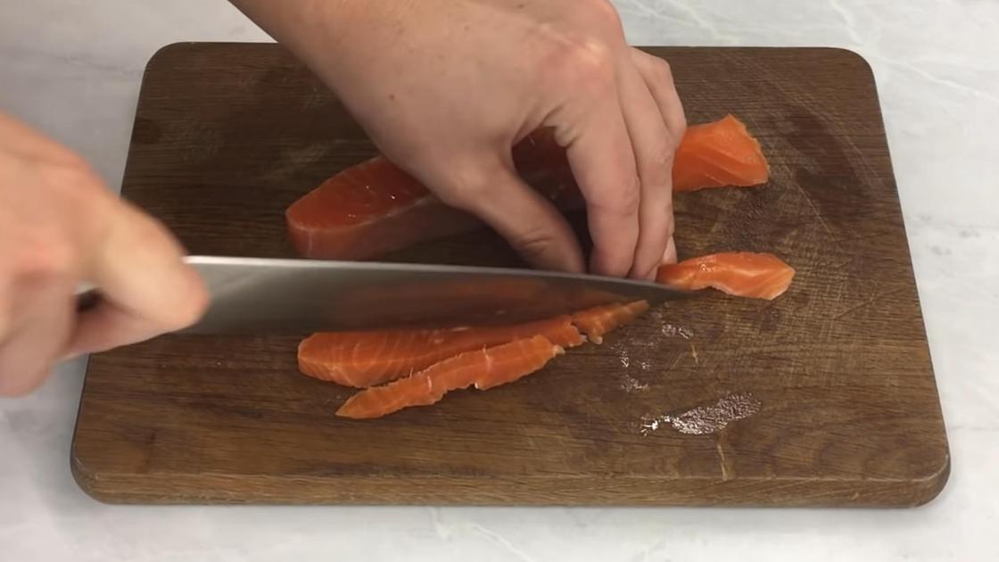 Слабосоленый лосось нарезают полосками на разделочной доске