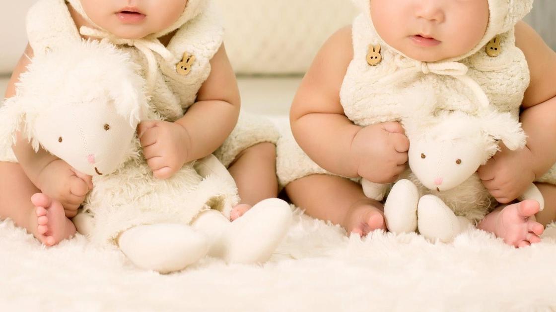 Дети-близнецы сидят на кроватке с игрушками