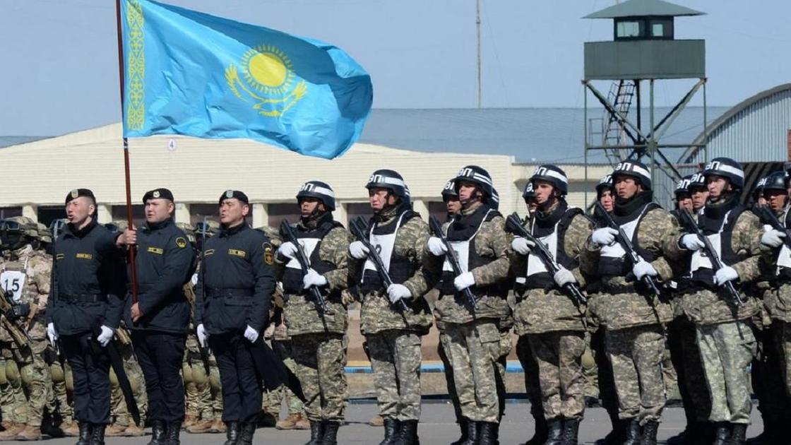 Люди в военной форме и с казахстанским флагом стоят в строю