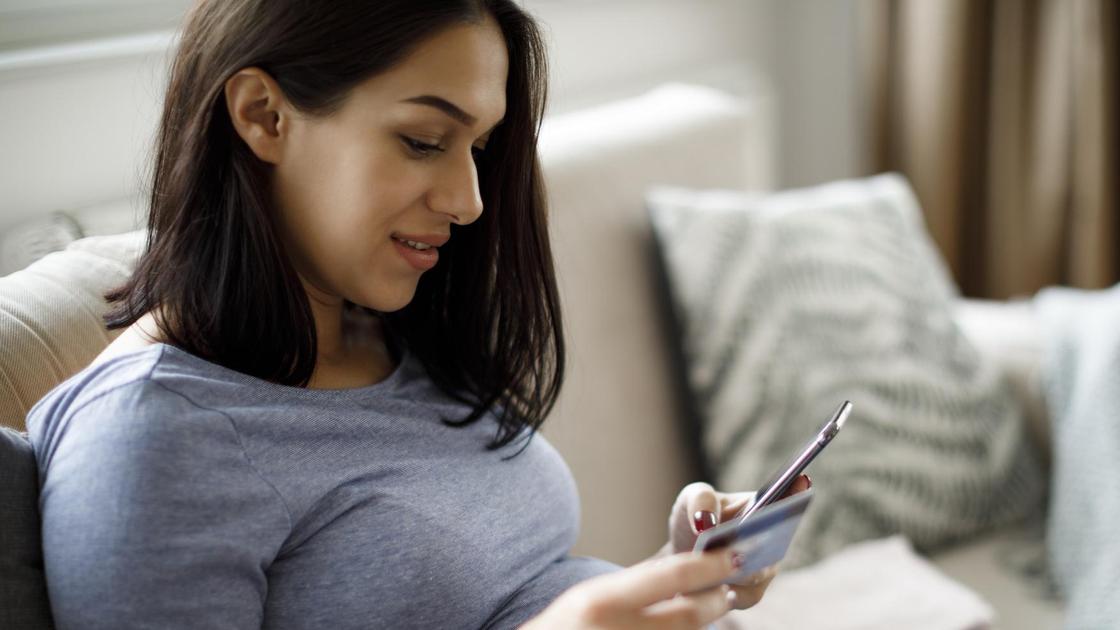 Беременная женщина смотрит в смартфон и держит платежную карту