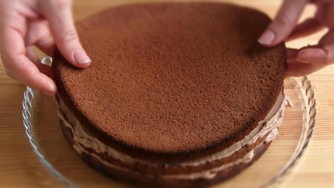 Женские руки выкладывают шоколадный корж на торт