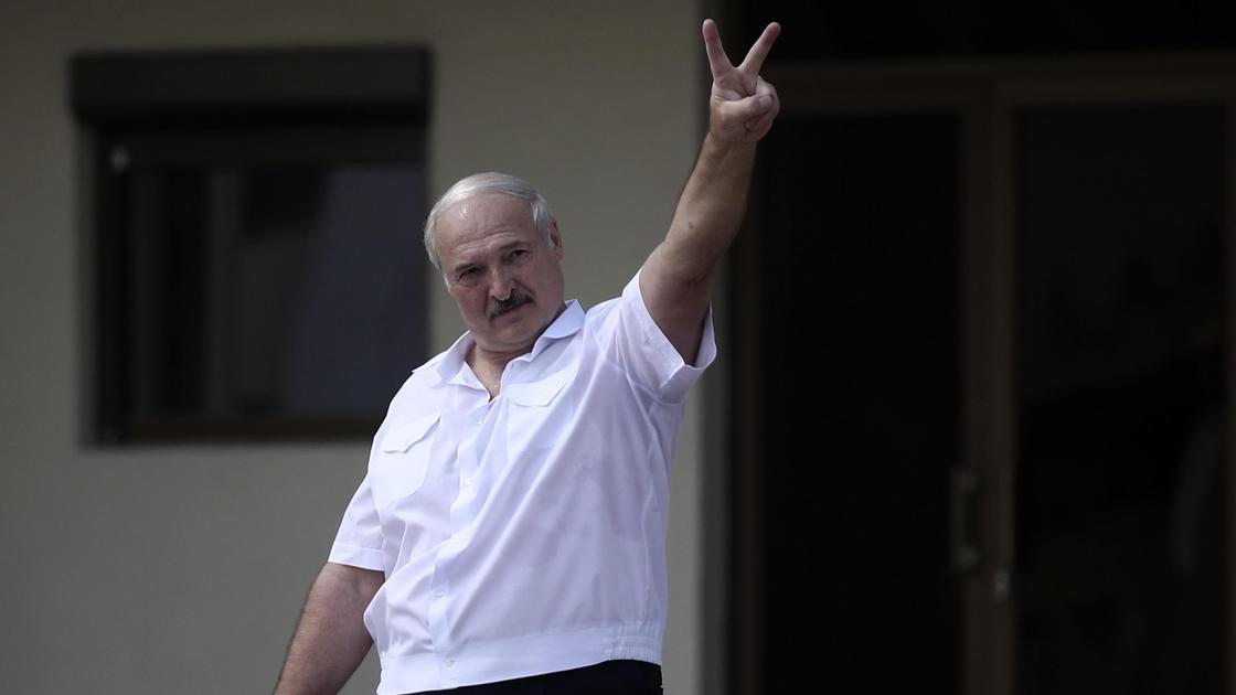 Александр Лукашенко в белой рубашке приветствует