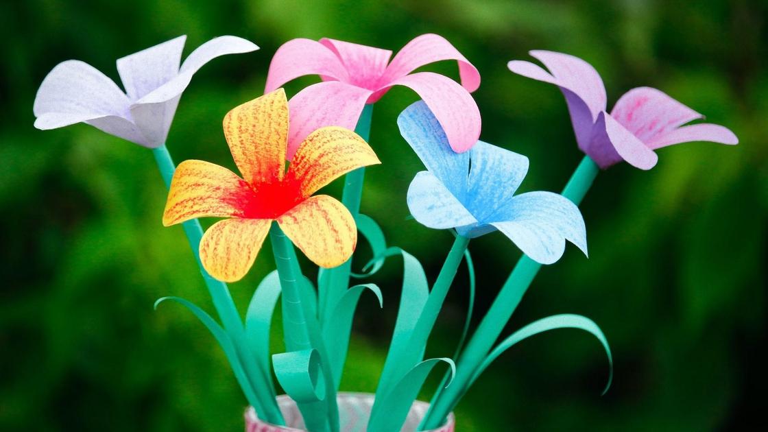 В вазе стоят разноцветные бумажные цветы. Стебли сделаны из зеленой бумаги с двумя длинными листиками