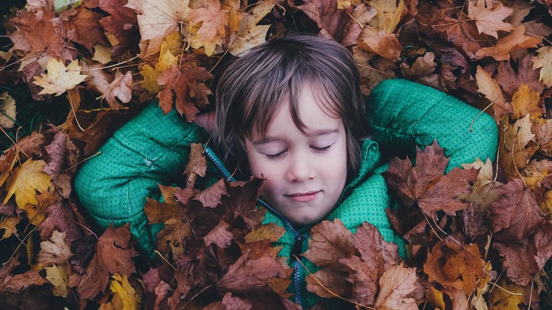 мальчик лежит в осенней листве