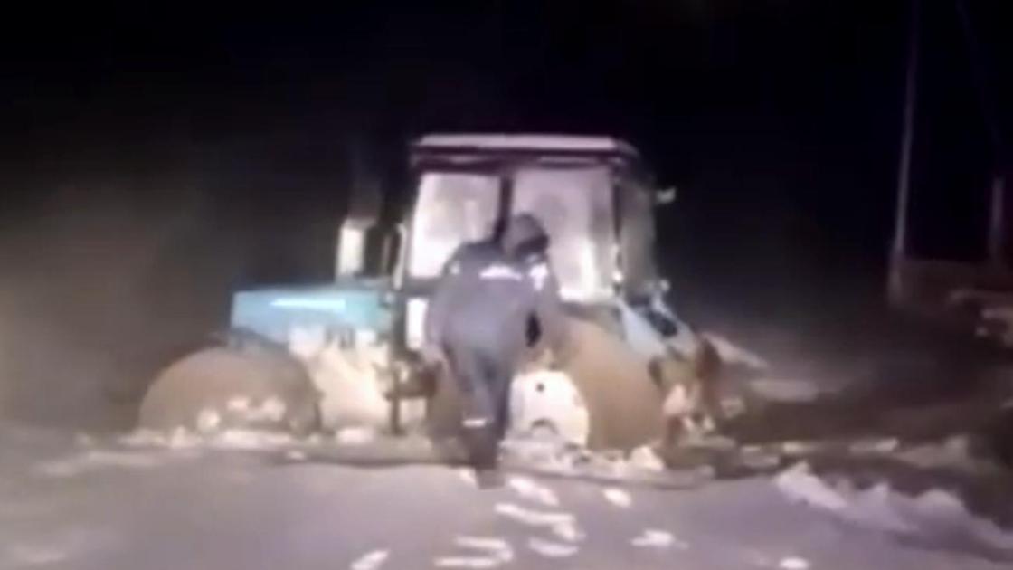 Спасатель стоит возле попавшего в снежный плен трактора