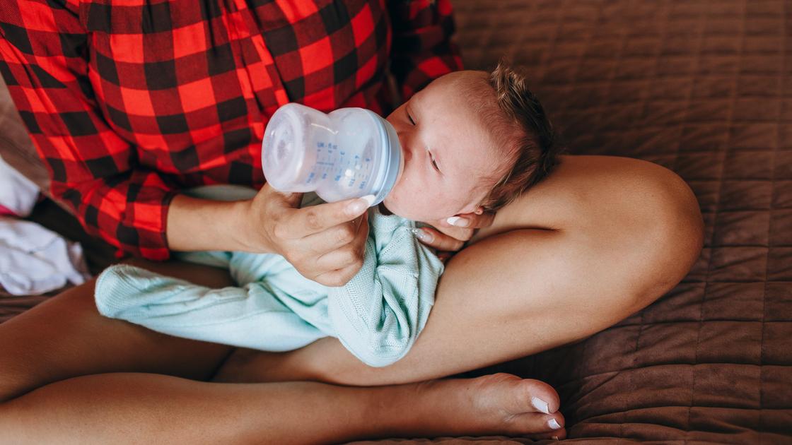Женщина кормит новорожденного из бутылочки