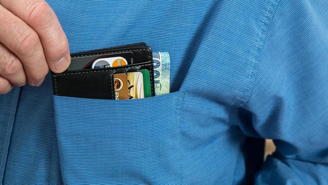 Мужчина кладет в карман портмоне с кредитными картами и деньгами