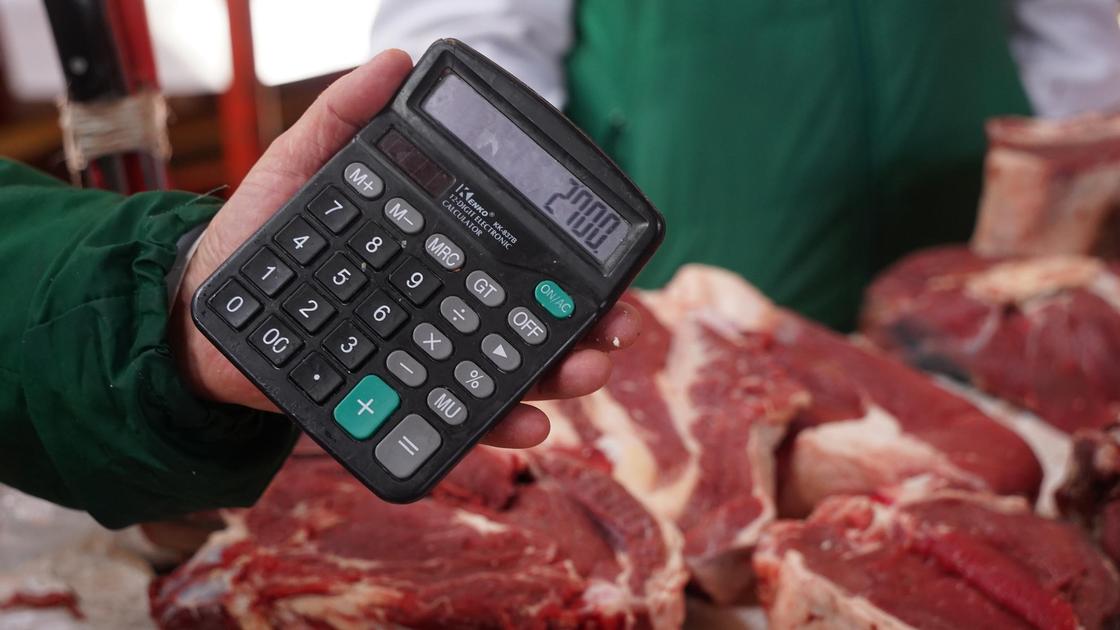 Продавец держит в руках калькулятор на фоне мяса