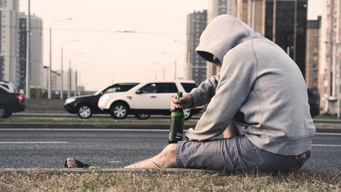 подвыпивший мужчина сидит на улице с бутылкой алкоголя