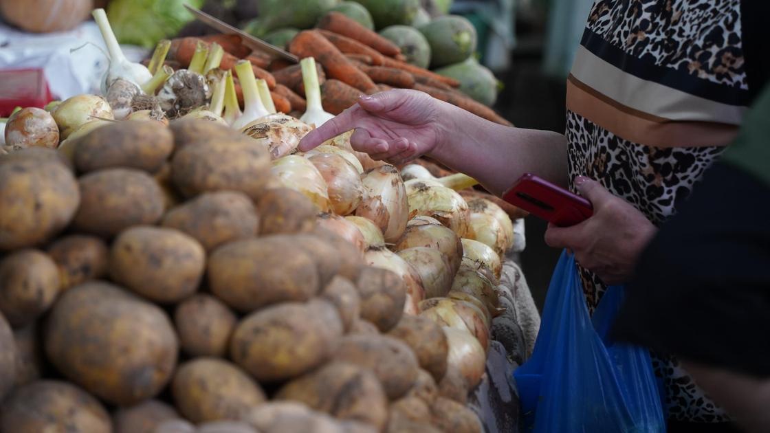Женщина покупает овощи на рынке