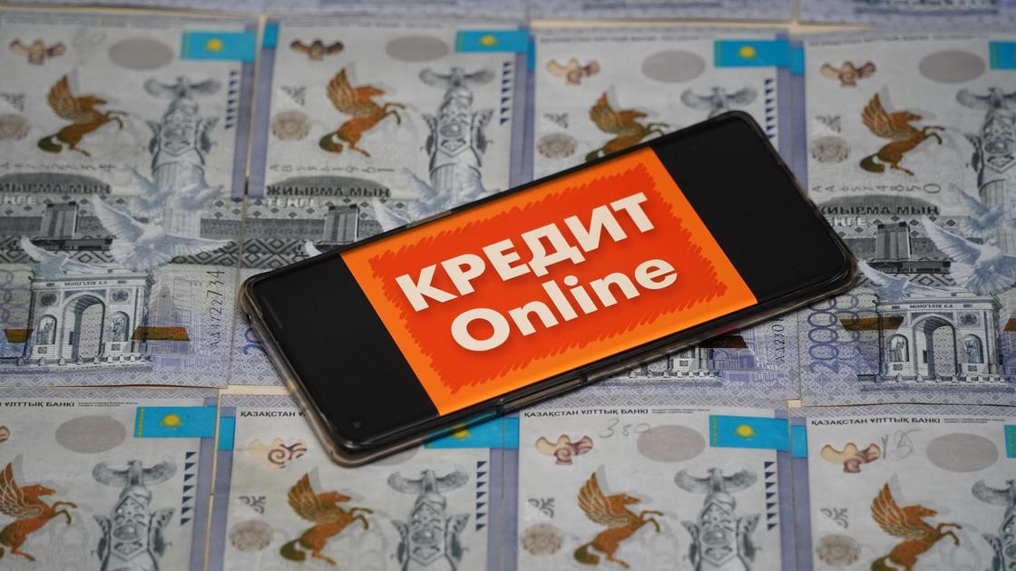 Телефон с надписью "Кредит онлайн" лежит на купюрах тенге