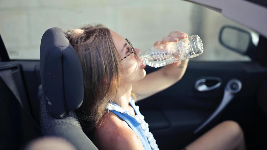 Женщина в машине пьет воду