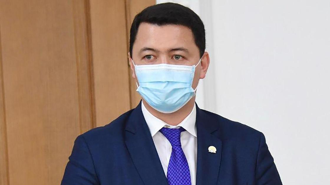 Камалжан Надыров в маске стоит в кабинете