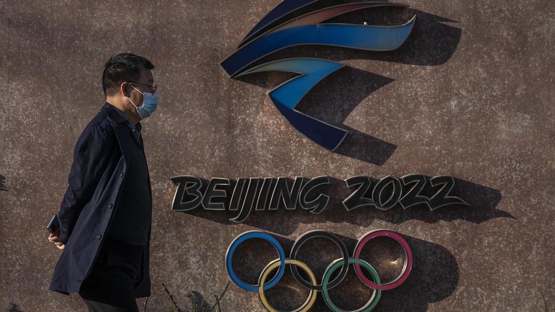 Мужчина идет возле стены с логотипом Олимпийских игр