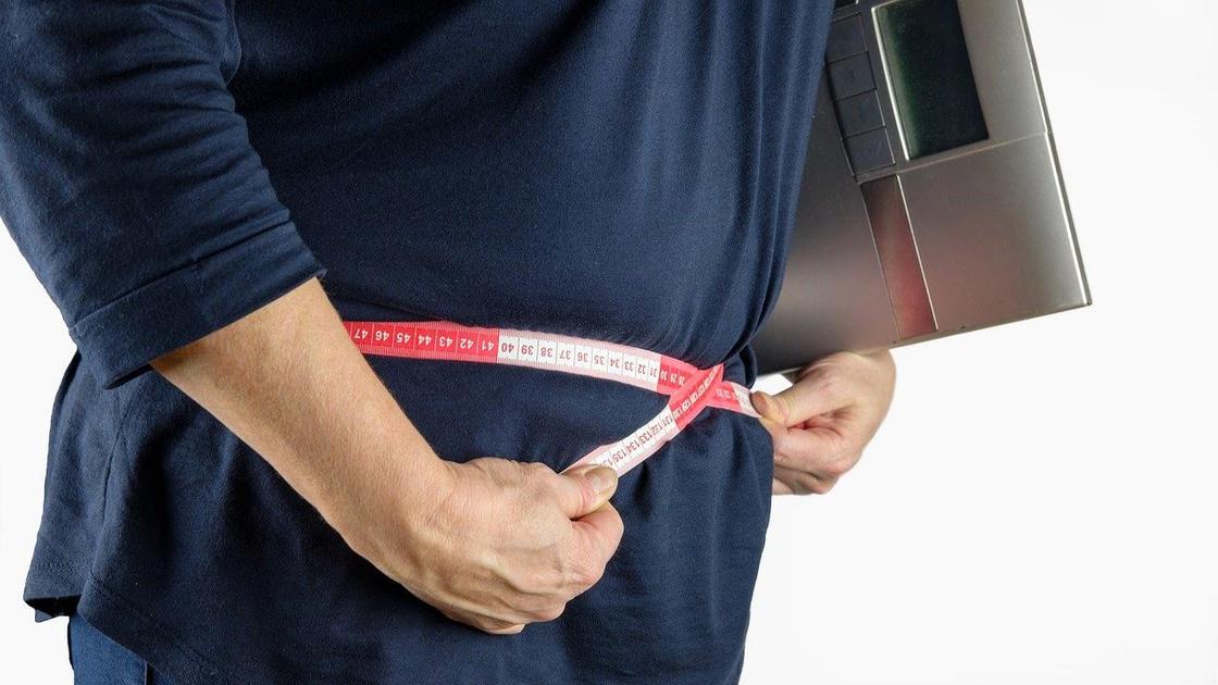 Человек измеряет талию с весами в руках
