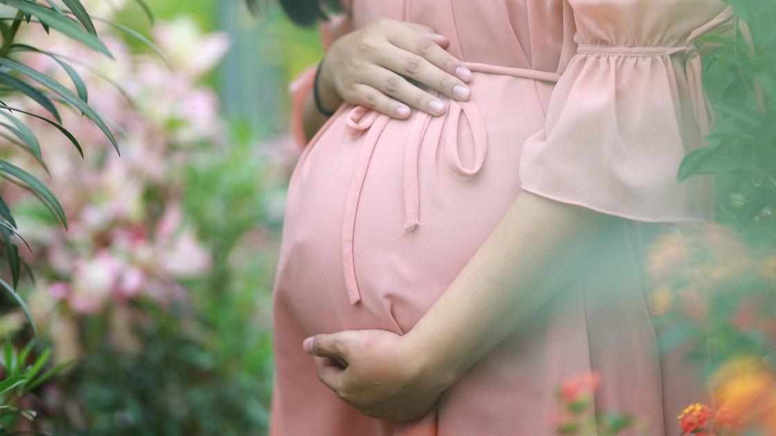 Беременная женщина обхватывает руками живот