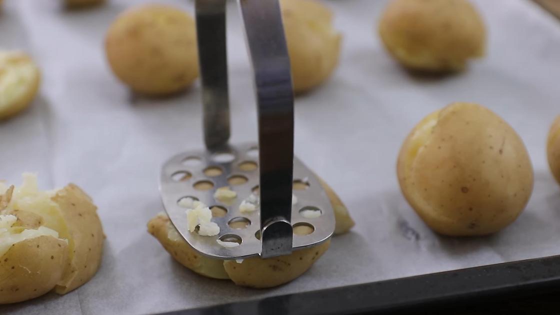 Сваренный картофель на противне разминают в лепешку толкушкой для пюре