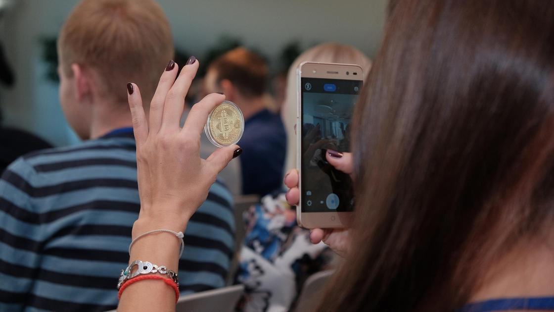 Женщина фотографирует монету биткоина на телефон
