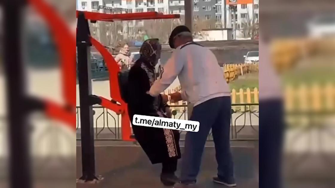 Пожилую женщину усаживают на уличный тренажер