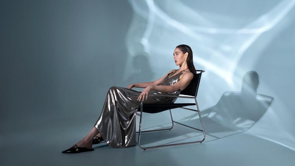 Девушка в длинном серебристом платье сидит на стуле