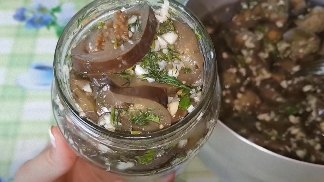 Кусочки баклажанов с чесноком и зеленью в открытой банке Кусочки баклажанов с чесноком и зеленью в открытой банке
