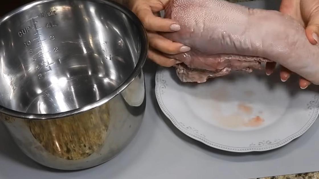 Женщина держит над тарелкой вымытый говяжий язык