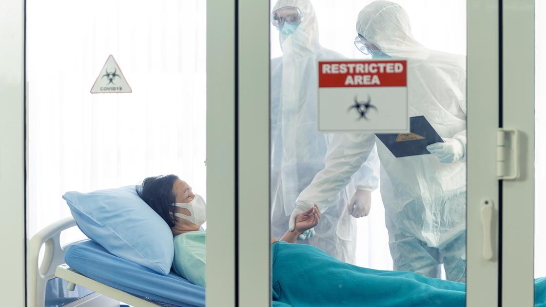 Двое медиков стоят у больничной койки пациентки за закрытыми дверями