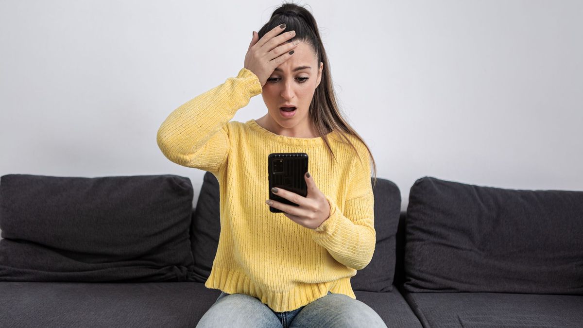 Девушка держится за голову и смотрит в свой телефон. Жертва мошенников