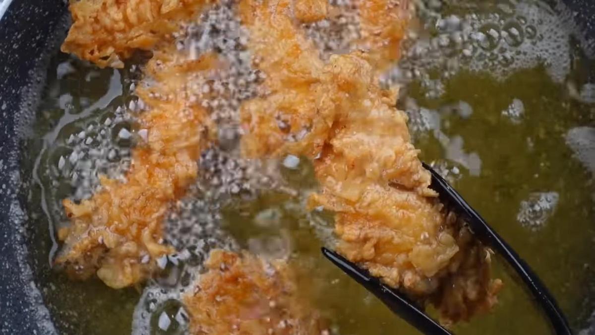 Кусочки куриного филе на сковороде переворачивают щипцами