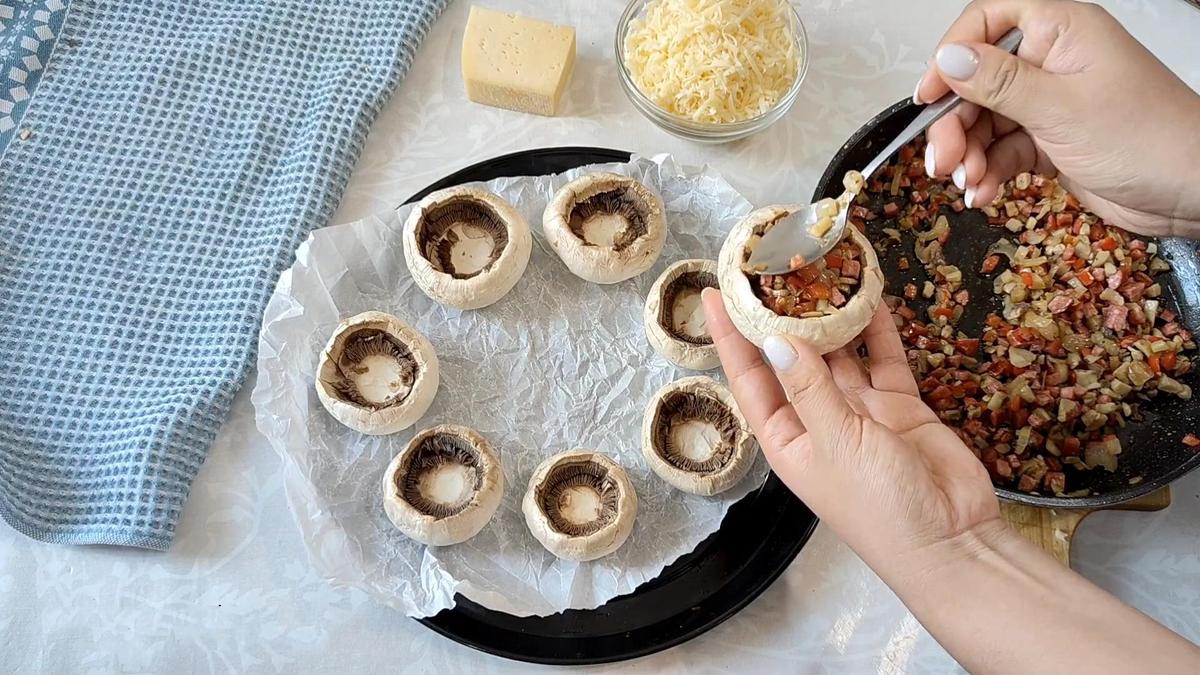 Шляпки шампиньонов наполняют начинкой из сосисок и овощей