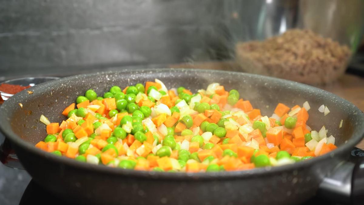 В сковороде жарится лук, морковь, зеленый горошек